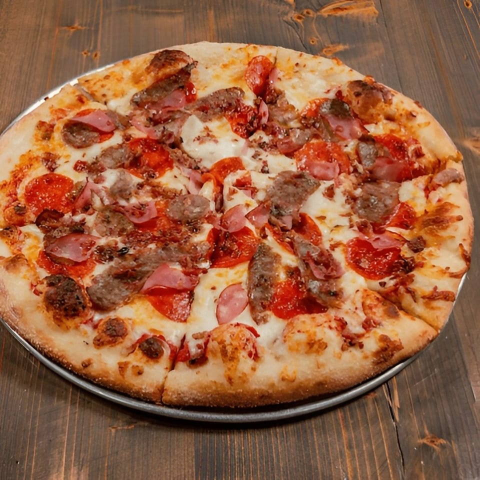 A whole meat lover's pizza with pepperoni, sausage, and ham on a wooden table.