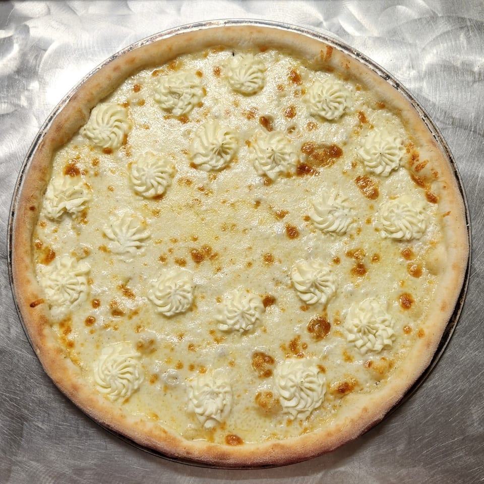 Round cheese pizza topped with piped cream swirls and golden browned spots on a metal baking tray.