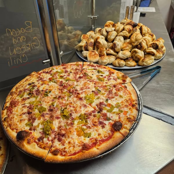 A large, sliced Joey's New York Pizza with bacon and green chili, next to a pile of garlic knots.