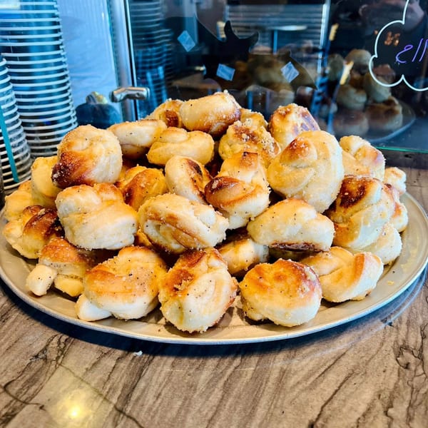 A large platter of golden-brown garlic knots, sprinkled with herbs, on a marble countertop.