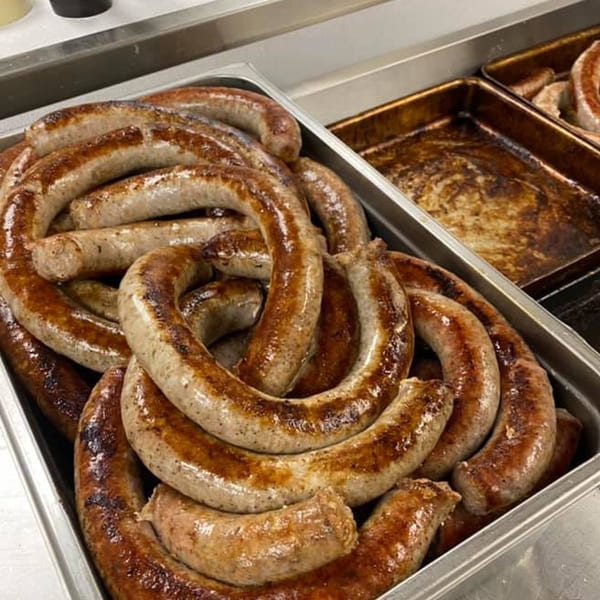 Many browned sausages in a metal tray, with an empty, greasy tray next to it.